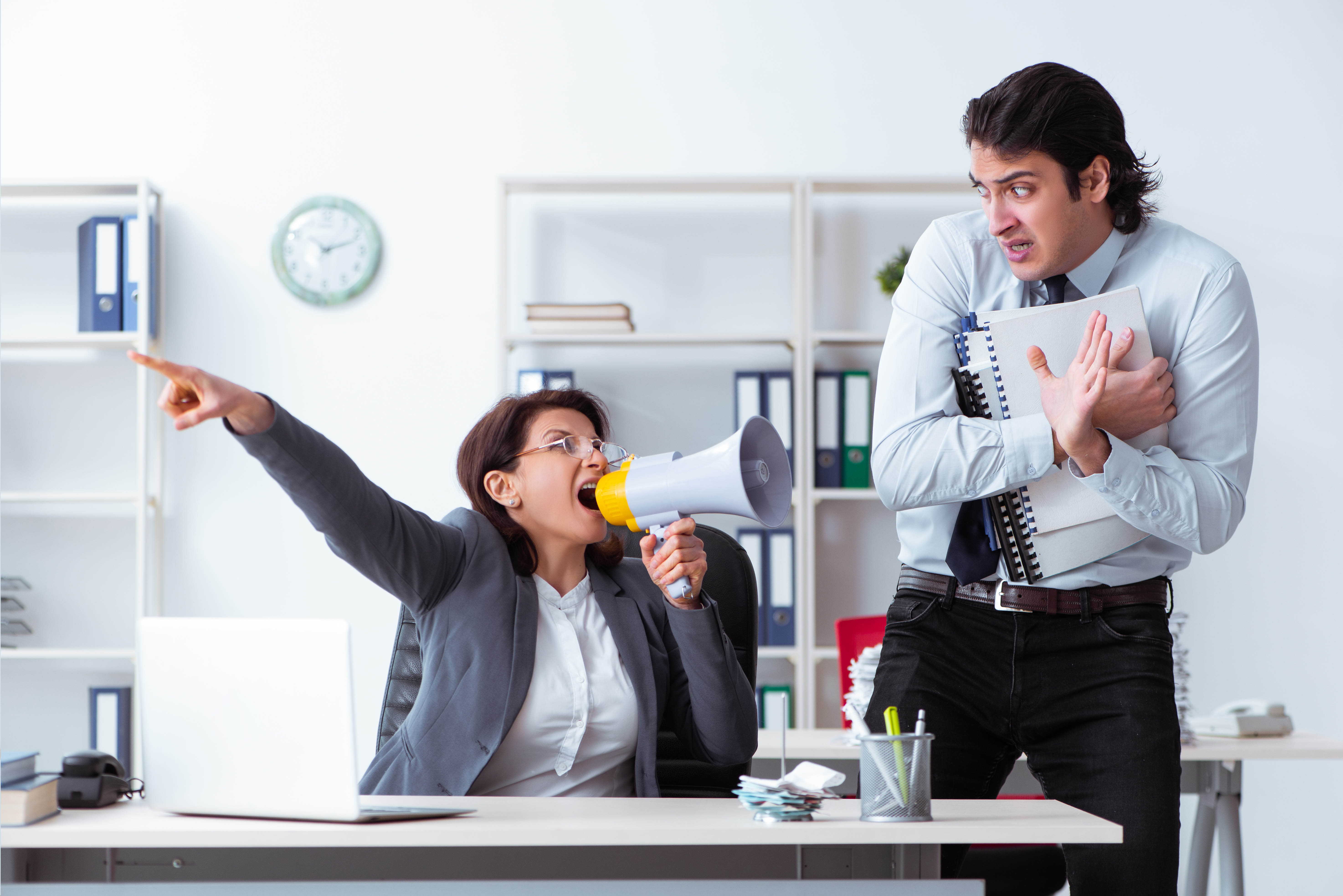 Woman yelling through a megaphone at a young male subordinate who is cowering away